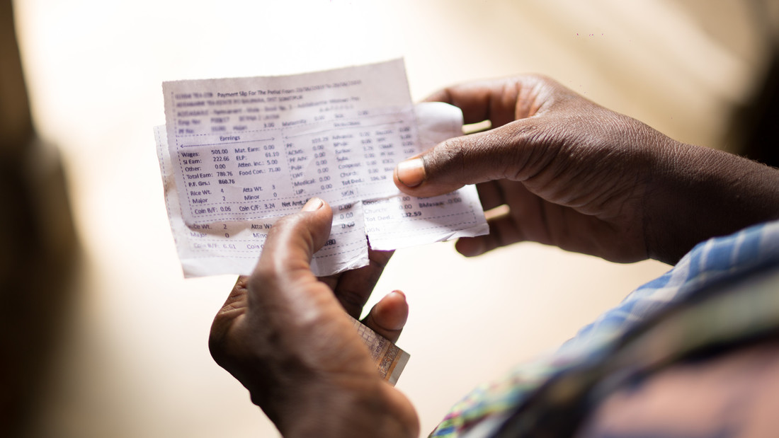 A woman tea plantation worker holds out her payment slip in her hand showing us the division of the payment and the daily wage.
